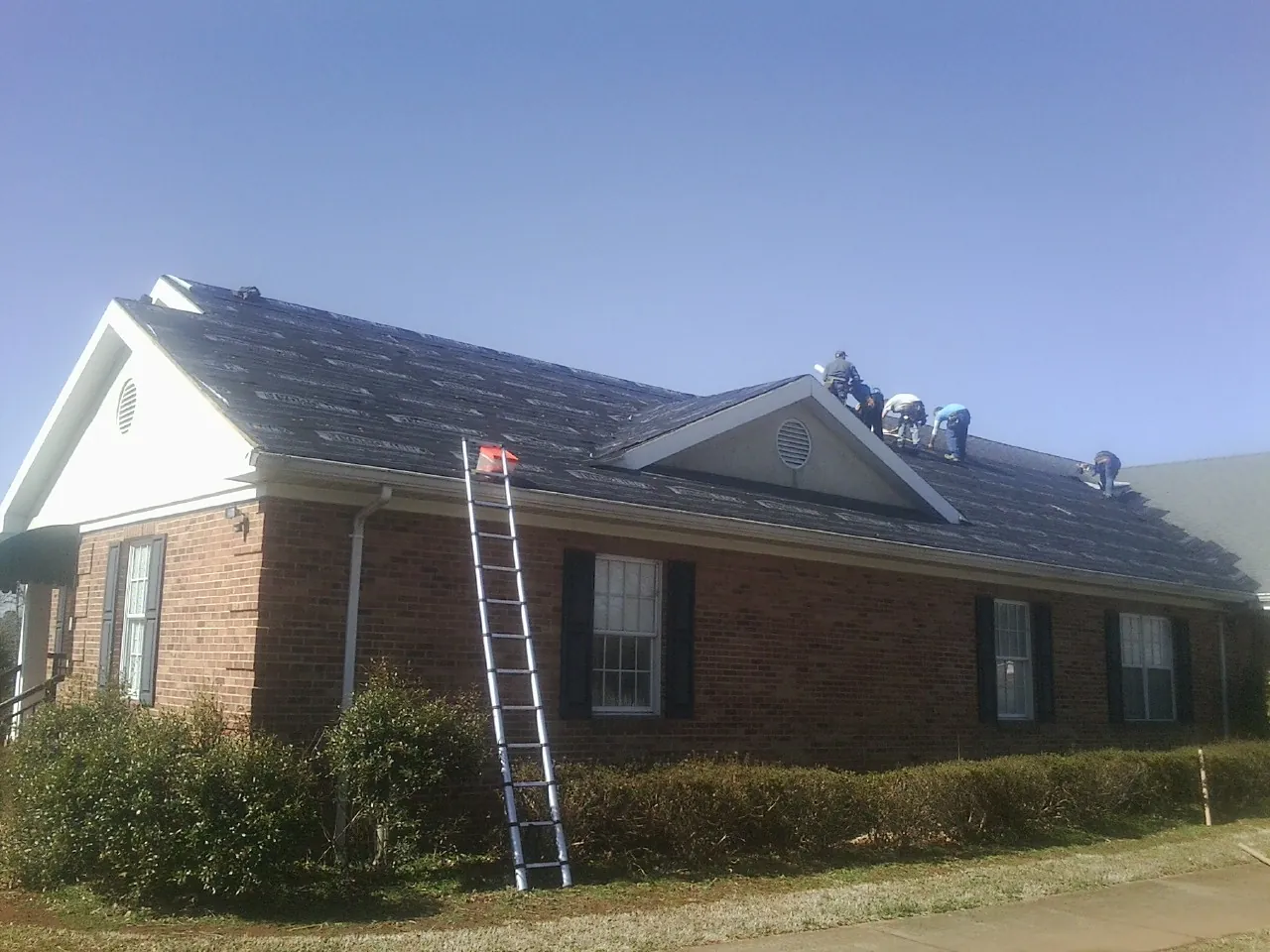 Crew tearing shingles off a brick ranch roof with a ladder set — Metal Roof Repair work by our crew in Brush Prairie