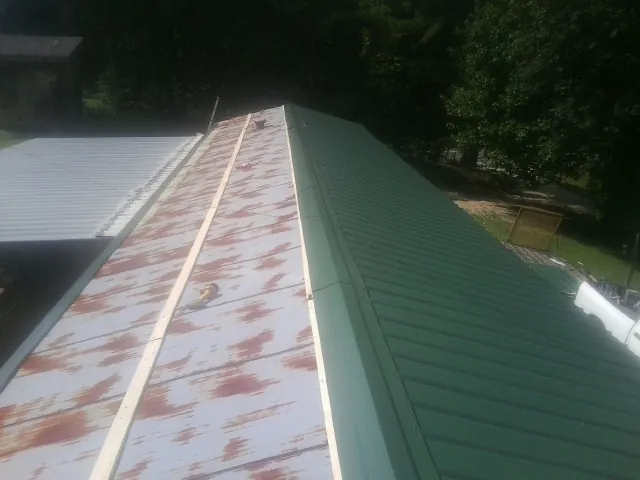 Old rusted panels beside newly installed green metal roofing — Wind Damage Roof Repair by Roofing Brothers in Brush Prairie