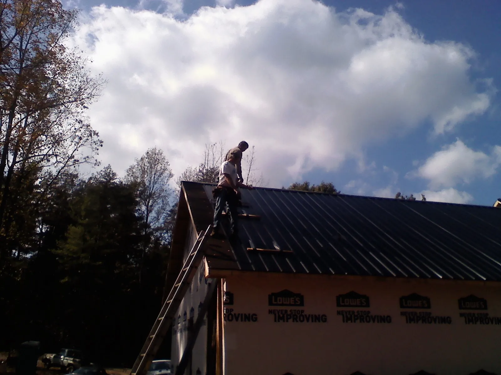 Roofer fastening dark metal panels high against a cloudy sky, from a Roof Inspection job in Brush Prairie