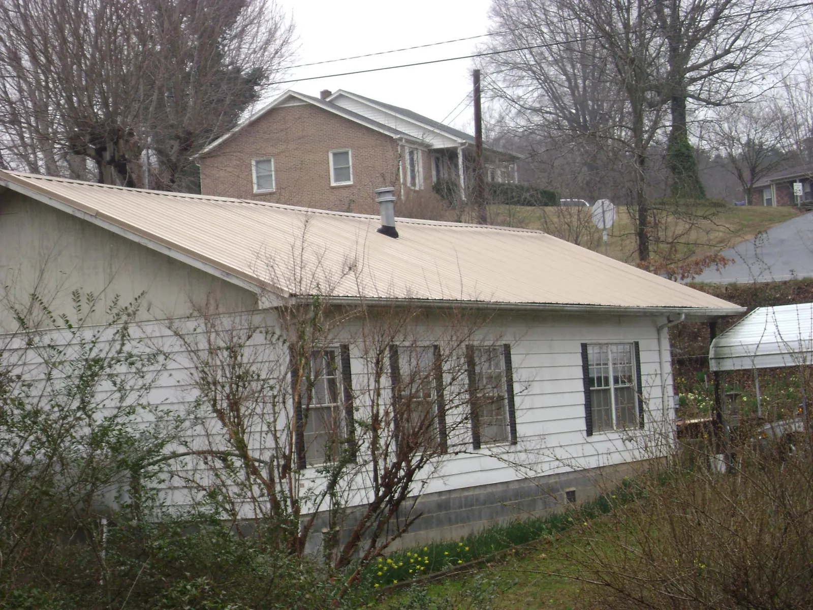 Tan metal roof on a white sided house set into a hillside — Commercial Roofing by Roofing Brothers in Brush Prairie